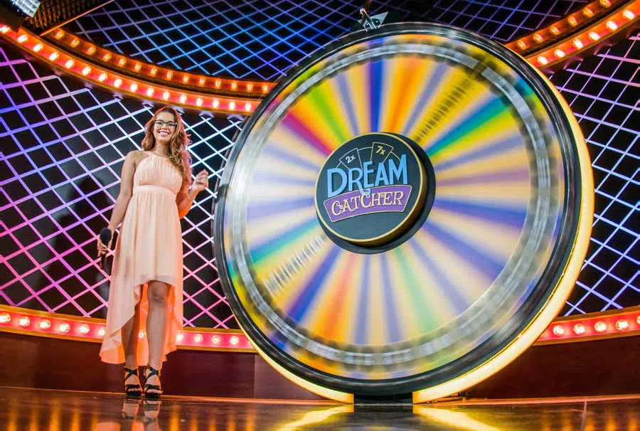 Dream Catcher Casino Game live dealer standing beside the spinning money wheel in Evolution Gaming’s studio.